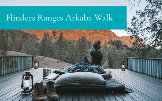 Two people relaxing on outdoor deck with lanterns viewing Flinders Ranges at sunset during Arkaba Walk experience